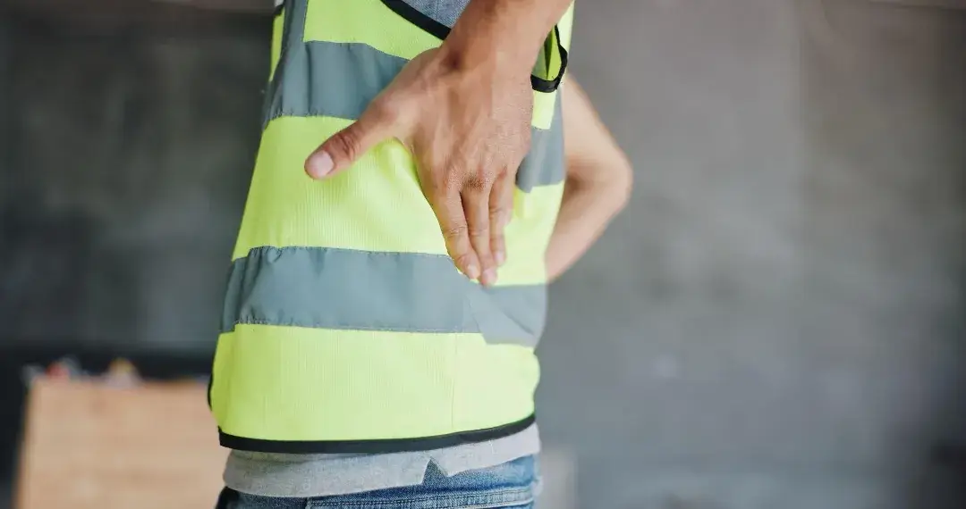 Construction worker holding lower back, representing a job-related injury covered by workers' comp.