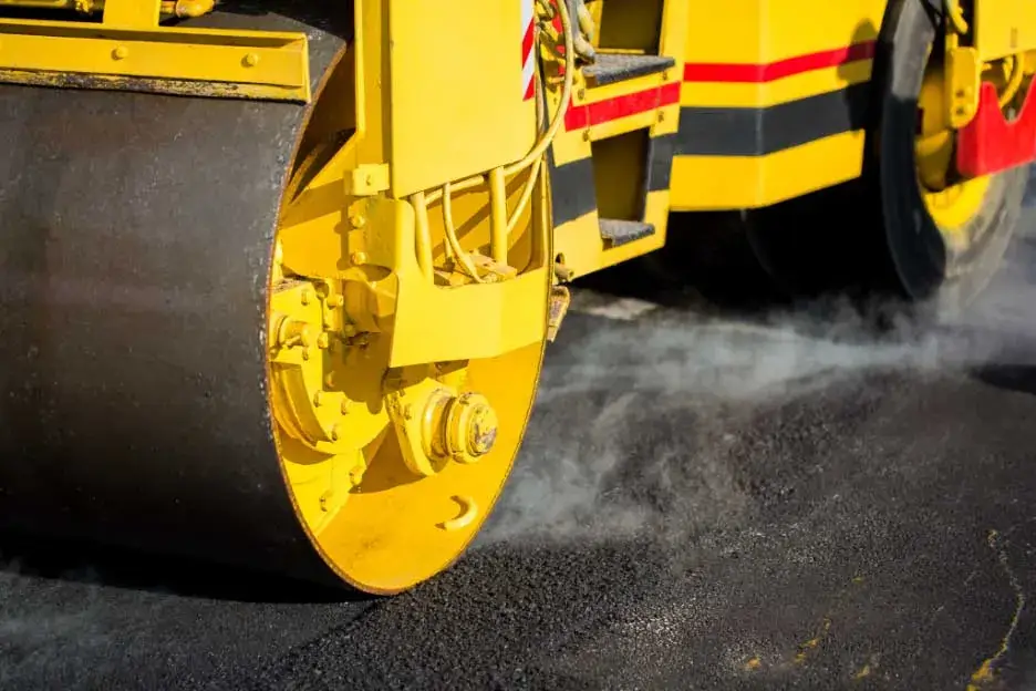 Licensed C12 contractor compacting newly placed asphalt using a road roller.